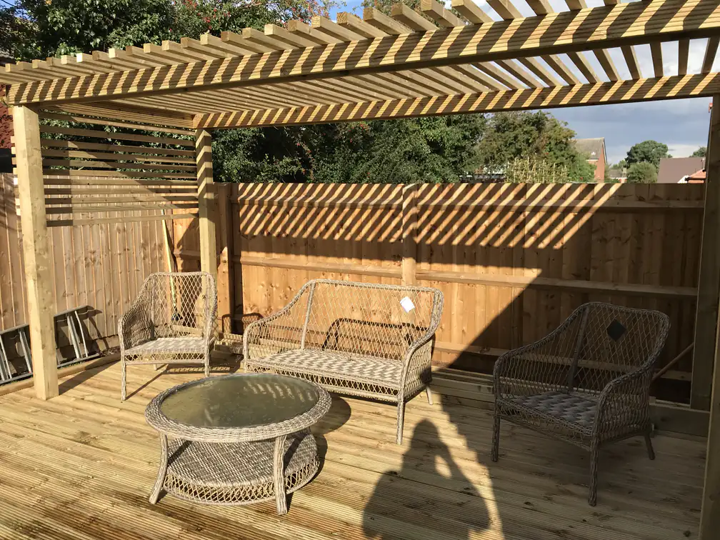 Timber pergola over new decking with rattan seating, a shaded outdoor room against warm brickwork.