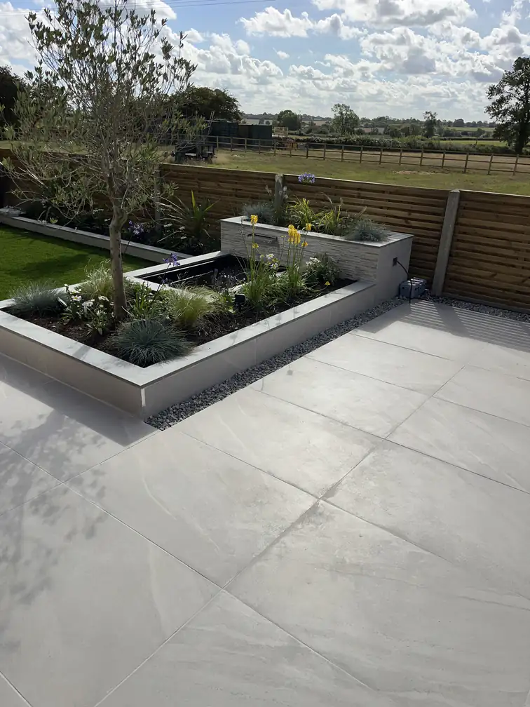 L-shaped porcelain planter wrapping a sunken pond within an expansive patio, sharp modern lines with lush planting.