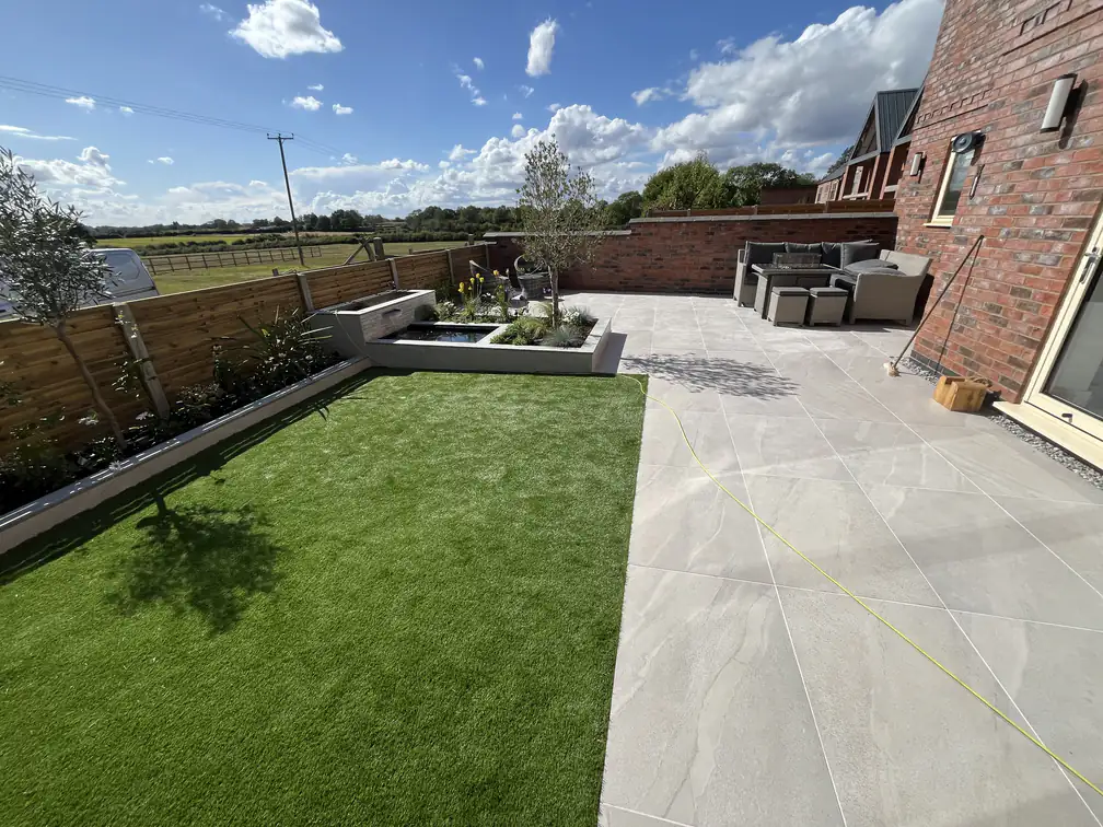 Artificial lawn and porcelain patio installation at a new-build home, a crisp zero-mow garden with countryside views.