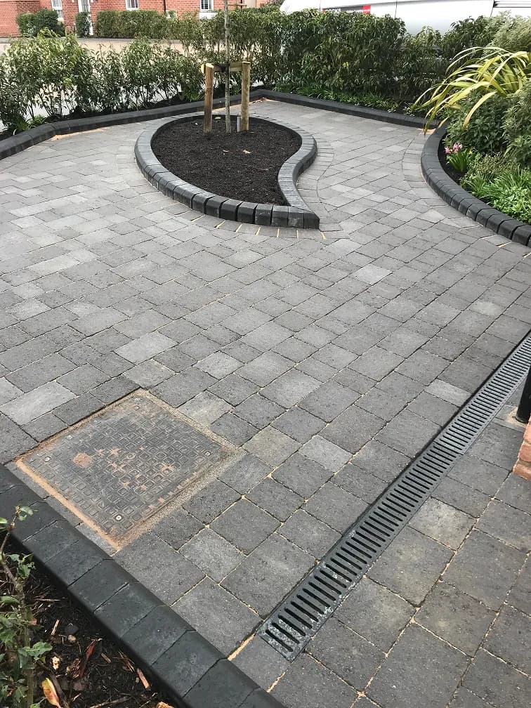 Curved block paved driveway with raised borders, dark edging stones and a drainage channel.