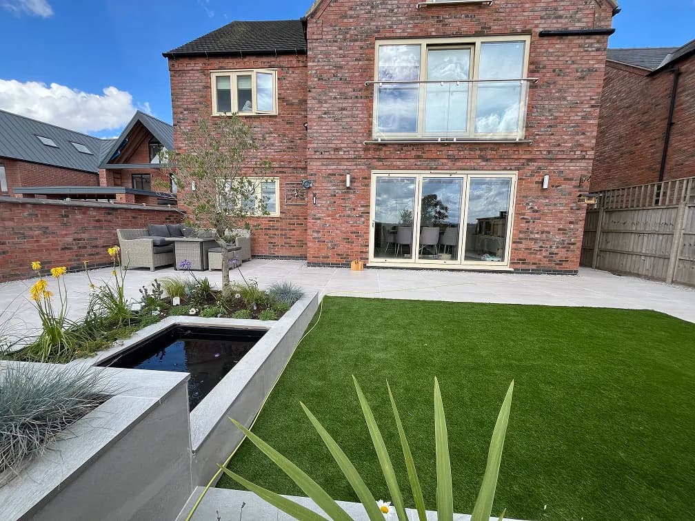 Modern back garden in Leicester with artificial grass lawn, patio and planting beds.