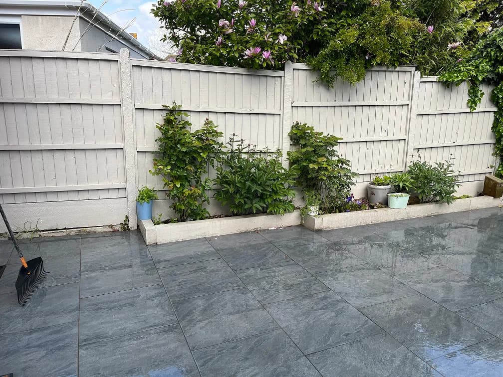 Large grey porcelain patio with raised planters, white garden fence, shrubs and glossy stone paving.