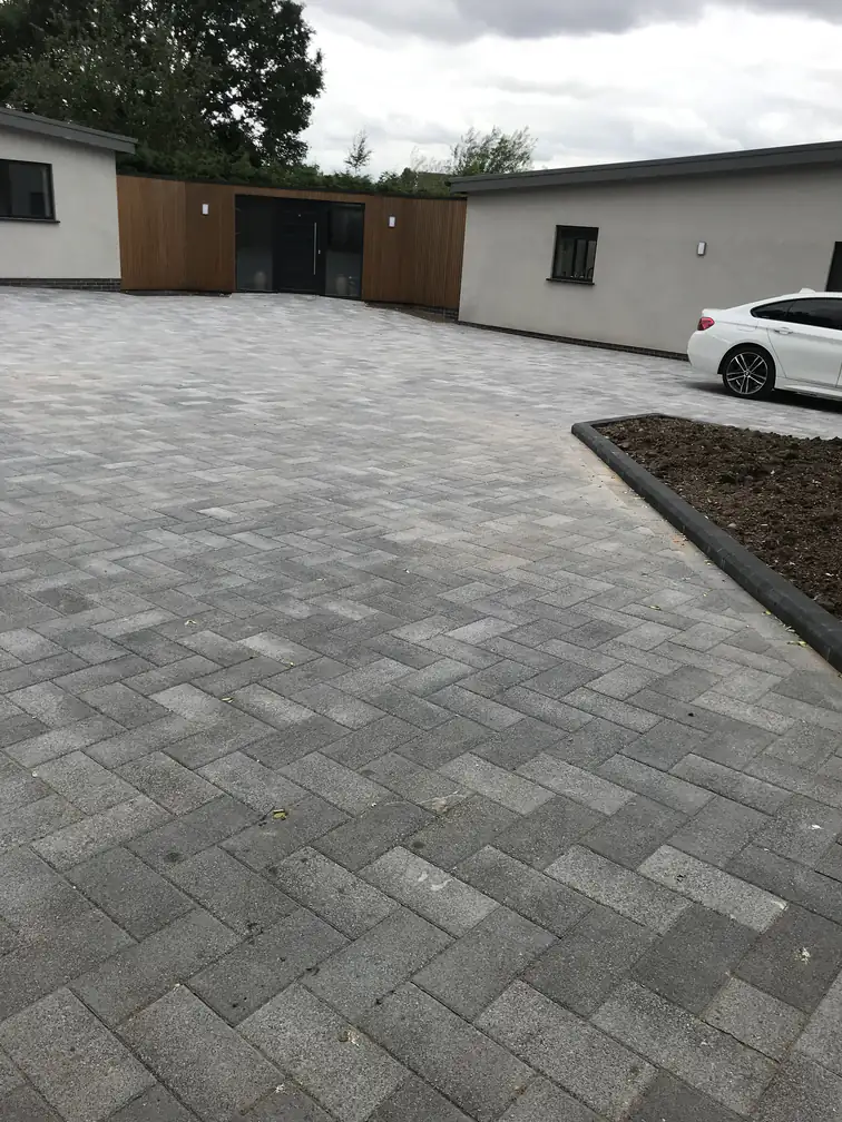 Block paved driveway and parking court beside a cedar-clad garage, modern materials with generous parking.
