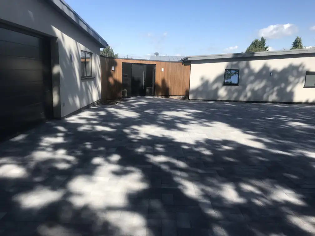 Charcoal block paving in dappled shade at a contemporary rendered property with cedar accents, understated and durable.