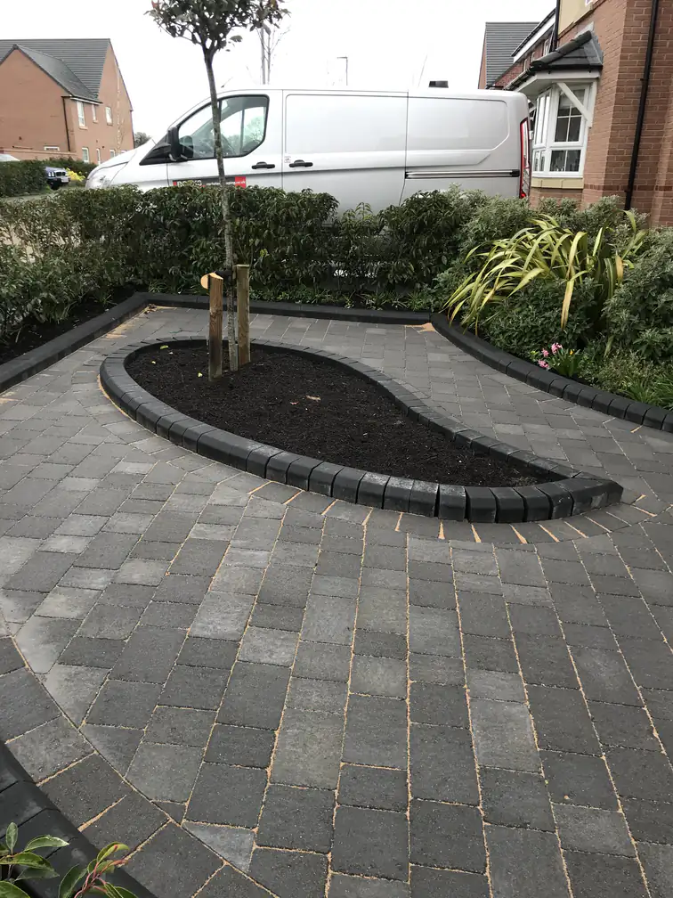 Charcoal block paving driveway laid in a fan pattern around a raised feature tree bed for a striking low-maintenance frontage.