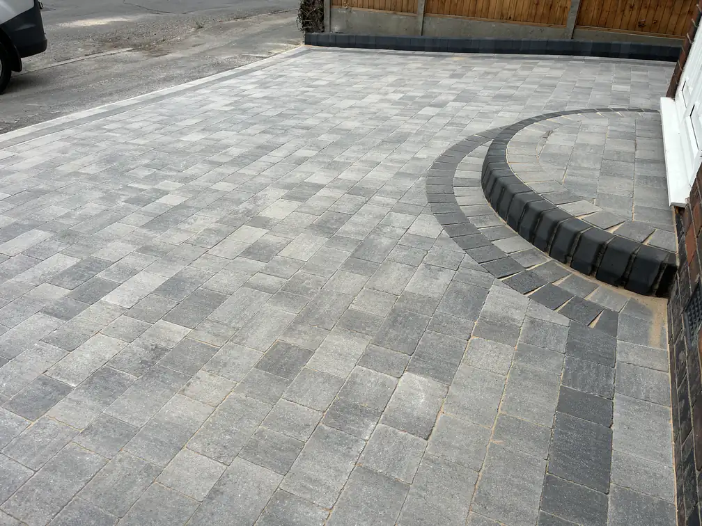 Grey block paving with a sweeping charcoal retaining step, precision detailing on a split-level driveway.