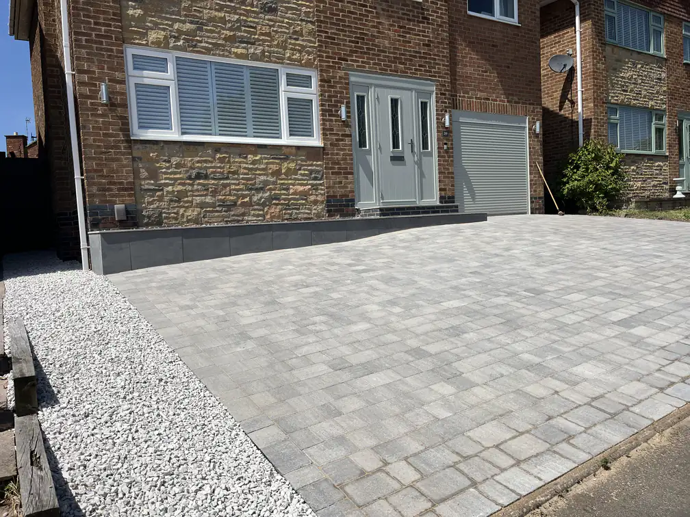 Silver-grey block paving driveway with white gravel border against a stone-fronted home for bright modern kerb appeal.