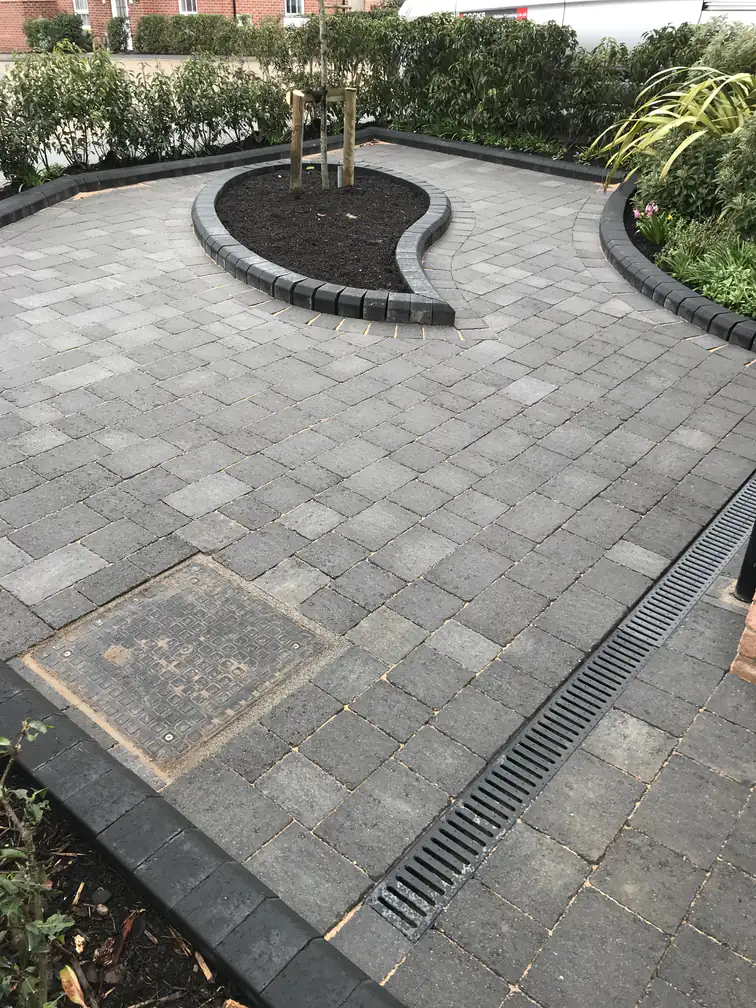 Tumbled block paving driveway with discreet drainage channel and curved island planter, combining practicality with smart design.