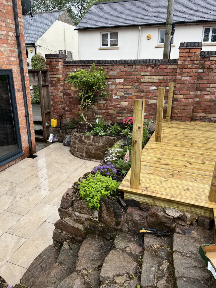 Timber decking and porcelain patio combination with reclaimed stone steps and planted rockery in a walled courtyard garden.