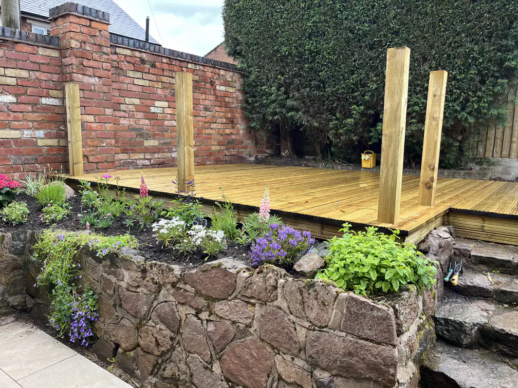 New timber decking framed by a rustic stone retaining wall planted with cottage flowers, a characterful walled-garden feature.