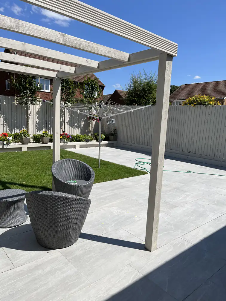 White-painted pergola over a porcelain patio with artificial lawn beyond, bright contemporary family garden.