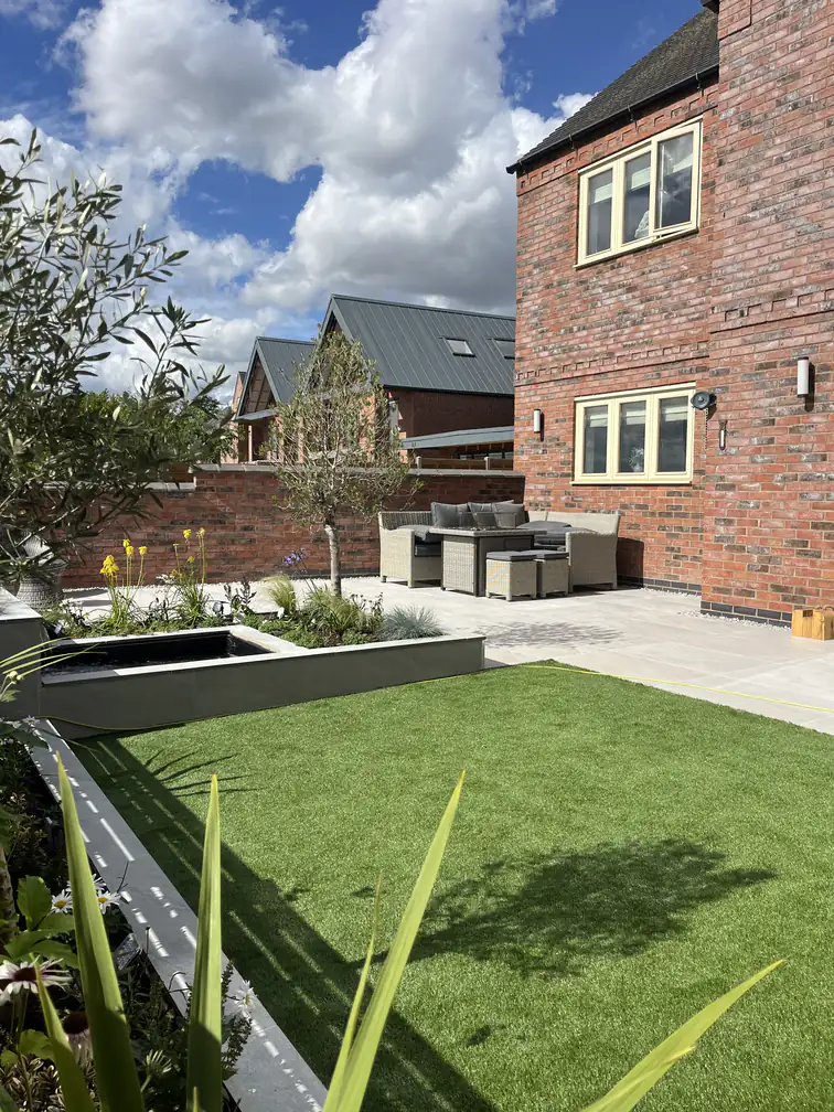 Complete new-build garden landscaping with artificial lawn, porcelain terrace, raised pond and lounge seating area.