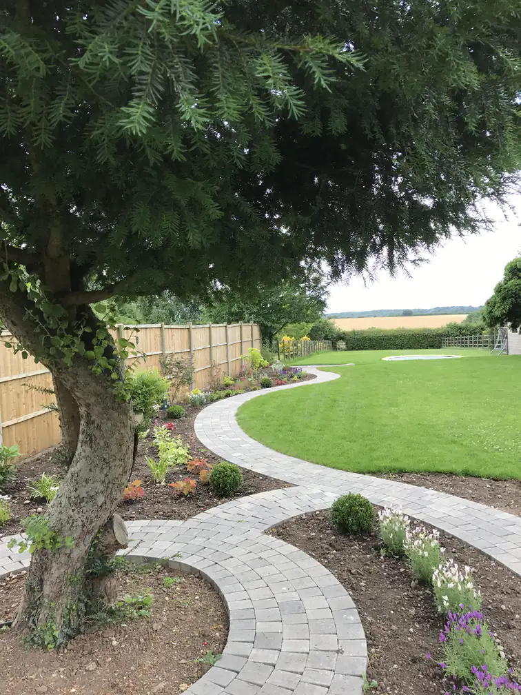 Garden path installation in tumbled block paving, sweeping in S-curves through a newly turfed lawn with planted borders.