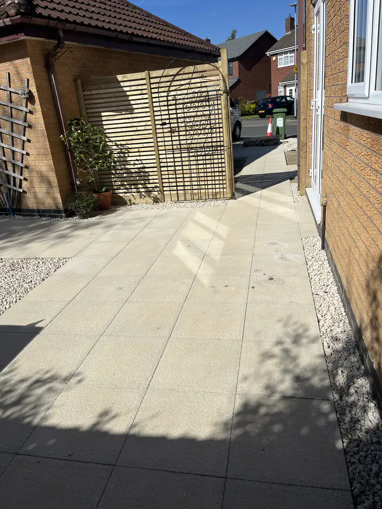 Buff paved side patio with slatted timber privacy screen and gravel borders, creating a tidy low-maintenance passage area.