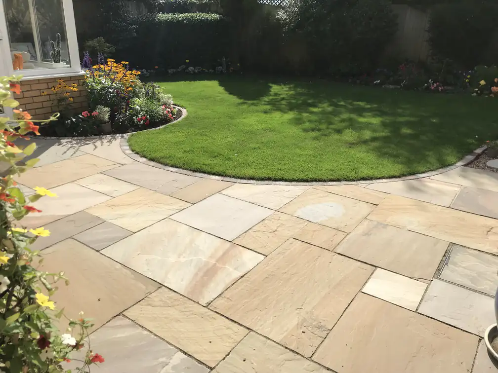 Indian sandstone patio sweeping around a circular lawn with colourful flower borders for classic garden charm.