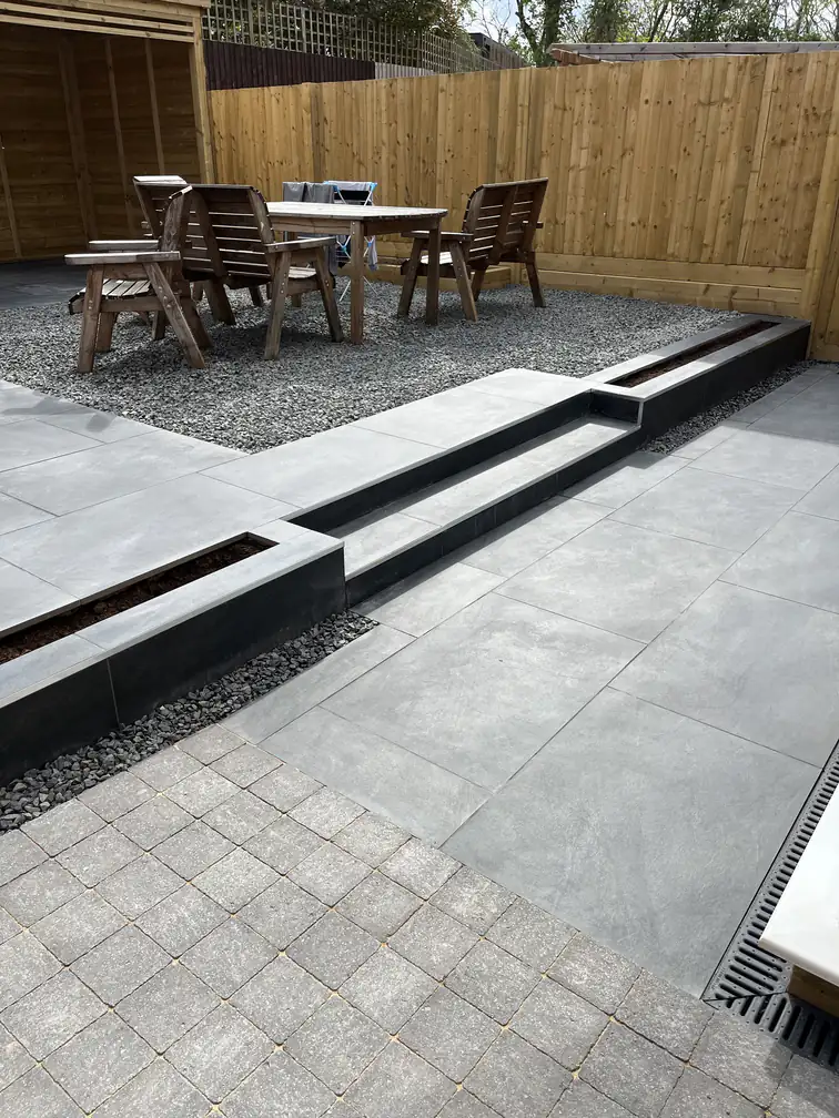 Dark porcelain patio stepping down to a gravel dining area with timber furniture, smart zoned outdoor living.