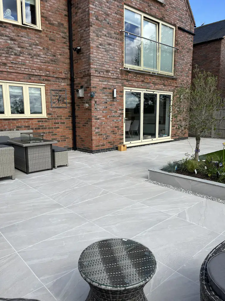 Garden terrace flowing from cream sliding doors past a raised olive tree planter, seamless indoor-outdoor living.