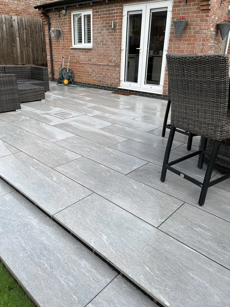Grey plank-format porcelain patio with rattan bar seating outside French doors, a sociable sun-trap terrace.
