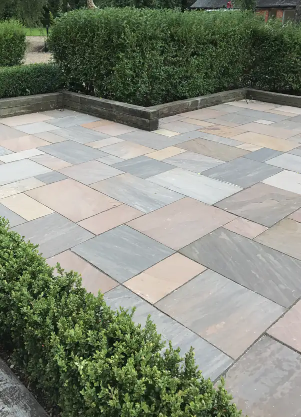 Indian sandstone patio with clipped box hedging and timber sleeper retaining wall for a classic low-maintenance courtyard.