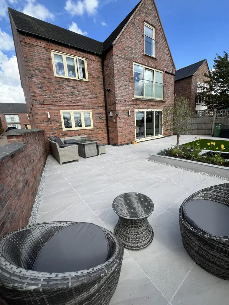 Porcelain patio seating area with rattan furniture beside a brick garden wall, a sheltered spot for morning coffee.