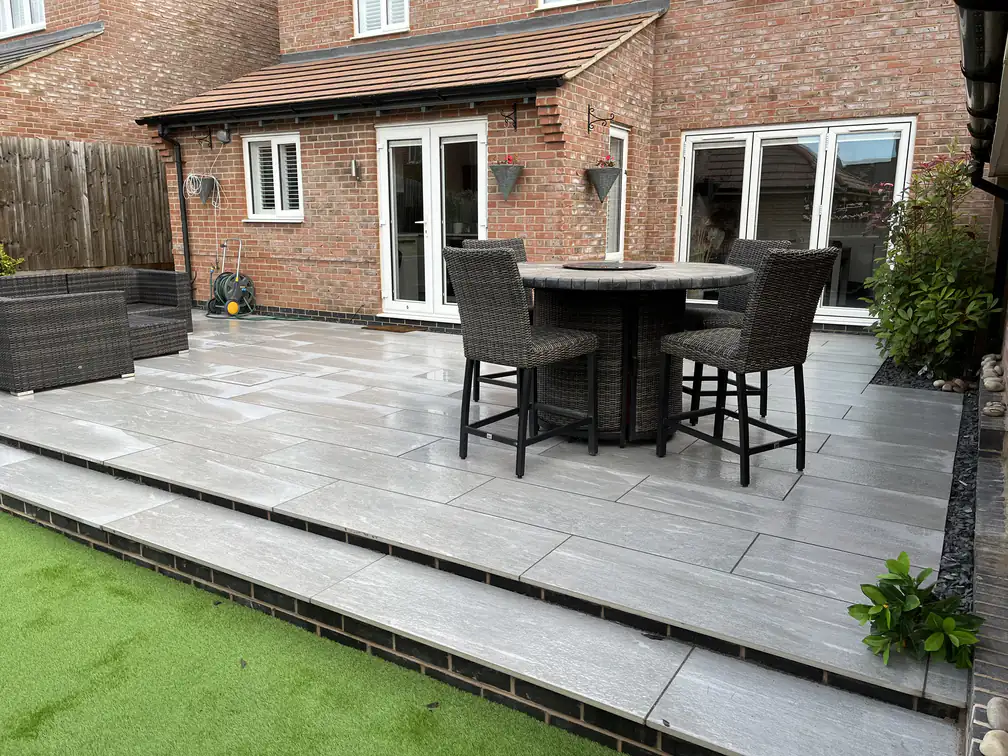 Porcelain patio with wide steps up to artificial lawn at a red-brick cottage, easy-care entertaining on two levels.