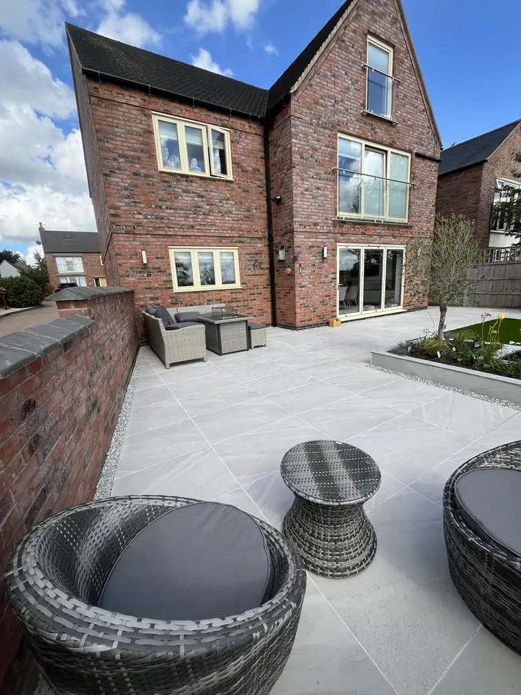 Porcelain terrace with rattan drum chairs beside a reclaimed brick wall, mixing modern paving with traditional character.