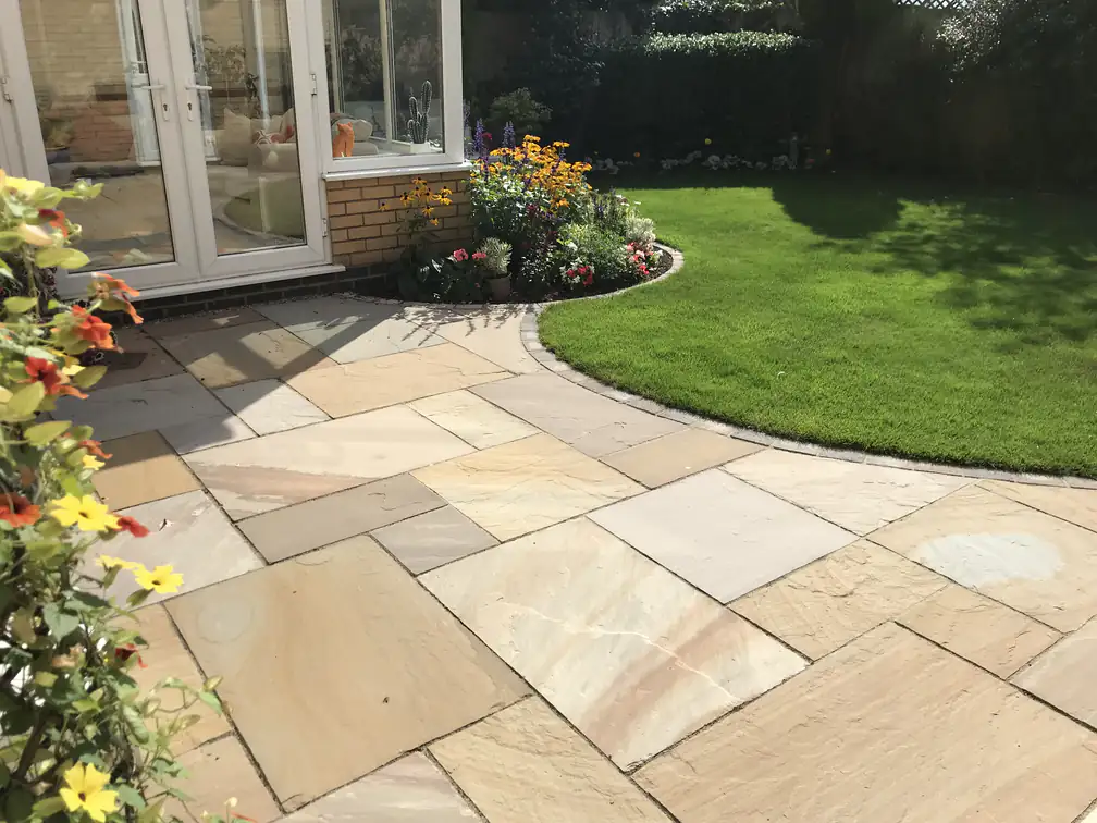 Indian sandstone paving with a curved lawn edge and vibrant planted borders, blending soft and hard landscaping.