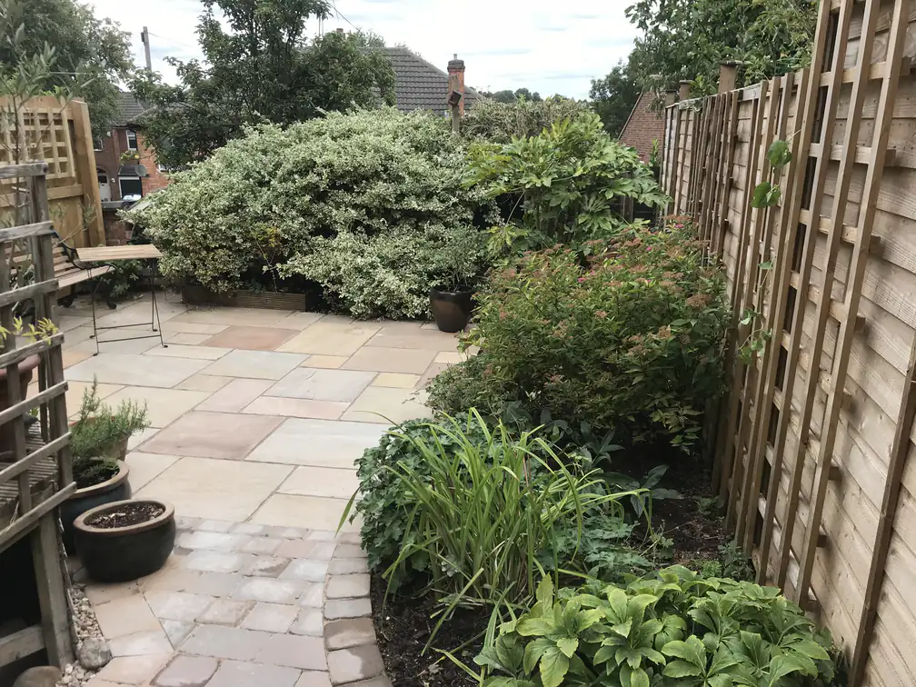 Riven sandstone patio settled into a mature cottage garden with trellis screening and established shrubs.
