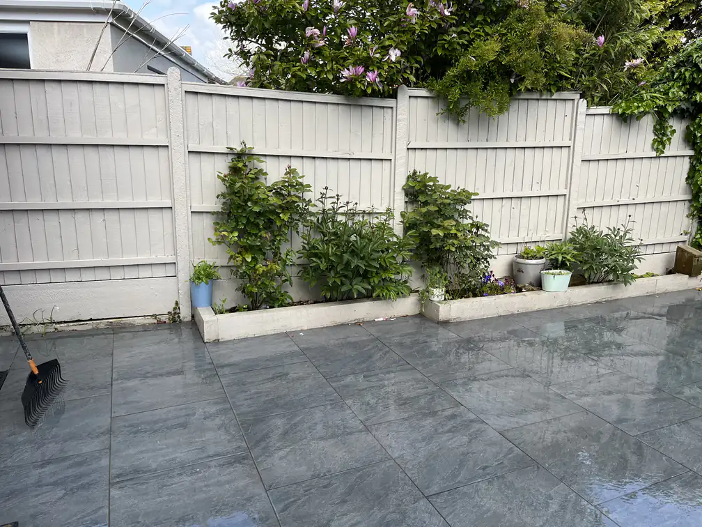 Slate-grey porcelain courtyard patio with planted border against white fencing, compact modern makeover.
