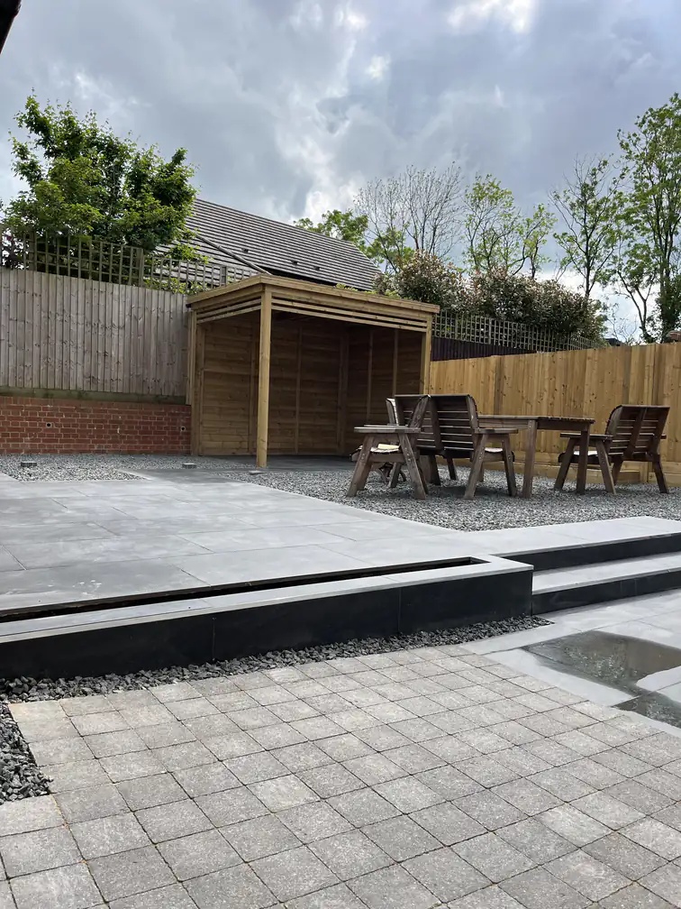 Two-tier porcelain patio with steel-edged steps and a timber gazebo dining shelter, sociable space whatever the weather.