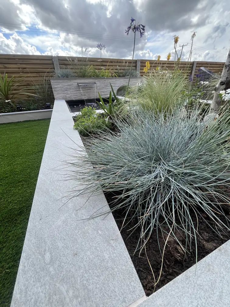Ornamental grass planting spilling from a raised bed beside artificial lawn walkways, structure with zero mowing.
