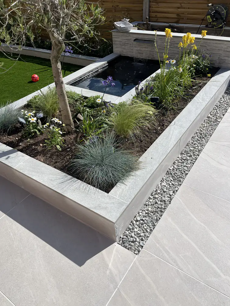 Raised porcelain planter beside a contemporary pond, softened with ornamental grasses and alpine planting.