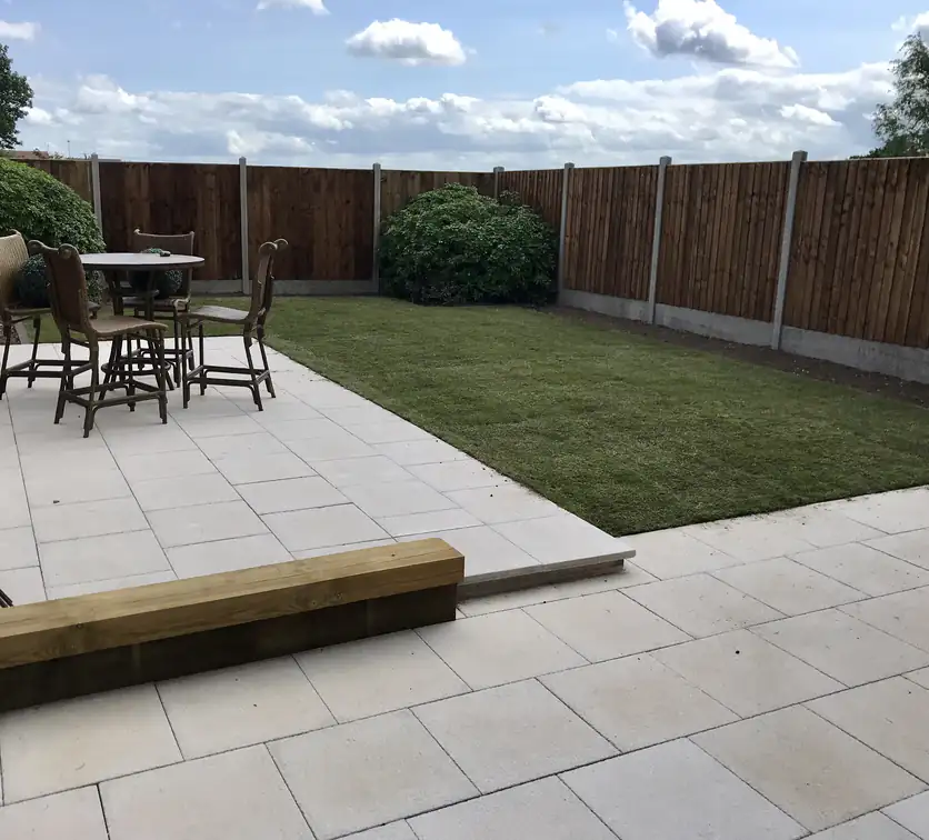 Patio installation in cream paving with fresh turf and an oak sleeper step, creating a bright family-friendly garden.