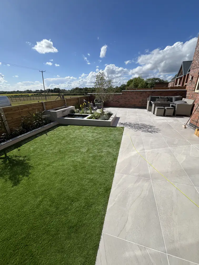 Porcelain patio flowing into artificial grass with open country views, contemporary landscaping that stays pristine year round.