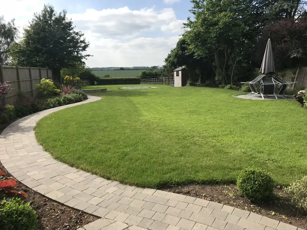 Sweeping lawn wrapped by a curved block path in a large country garden with open field views.