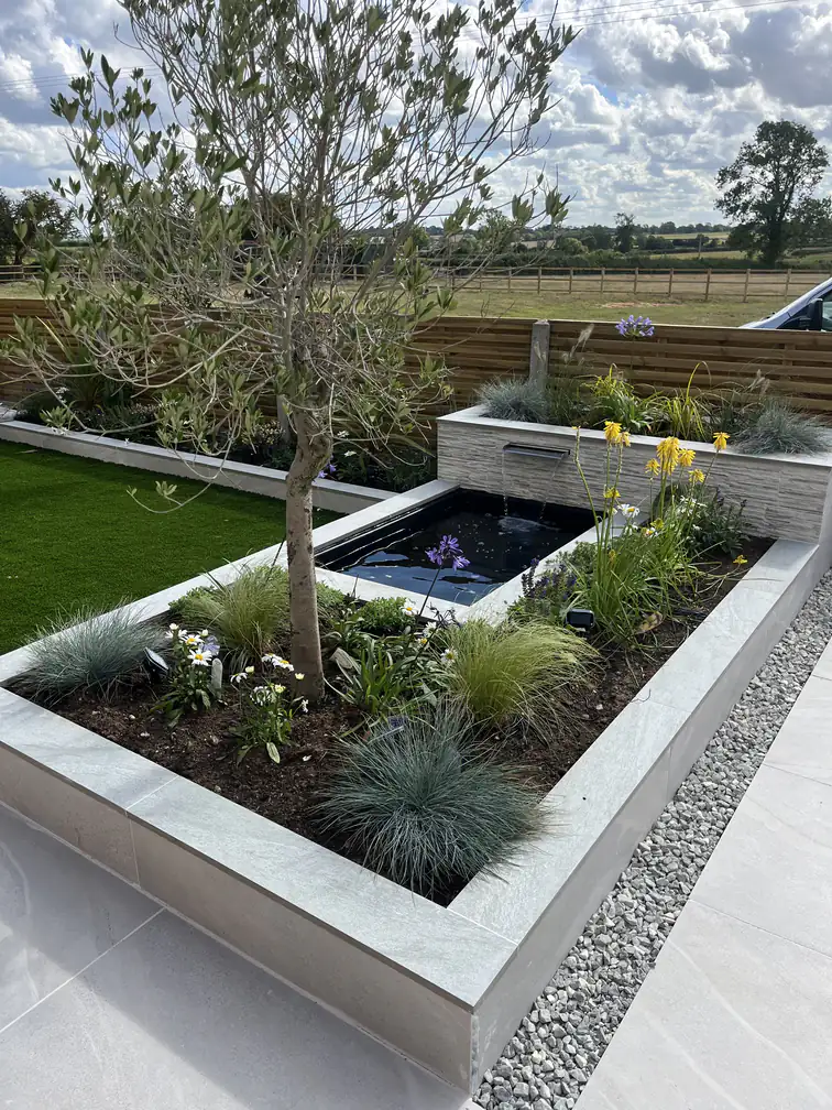 Raised pond and planter filled with daisies, grasses and kniphofia, colourful low-maintenance summer interest.