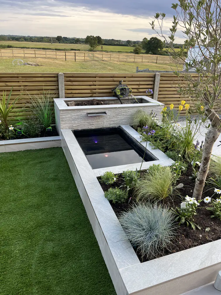 Modern raised pond with waterfall blade and integrated planters in porcelain stone, a striking low-maintenance centrepiece.