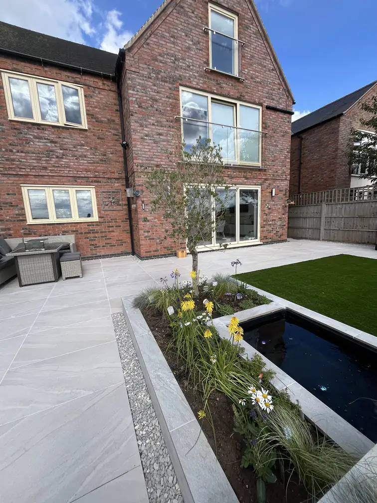 Sunken pond edged in porcelain with daisies and ornamental grasses spilling over, softening crisp modern landscaping.