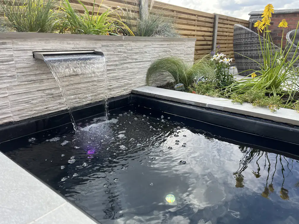 Water blade feature and pond softened with ornamental grasses and daisies, sound and movement for a modern garden.